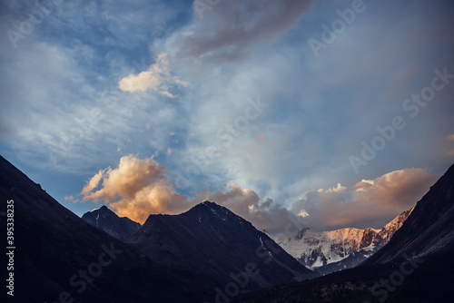 Amazing vivid landscape of sunset with awesome mountain silhouettes and orange clouds. Atmospheric highland scenery with great silhouettes of mountains under dawn sky. Snowy mountains in orange clouds