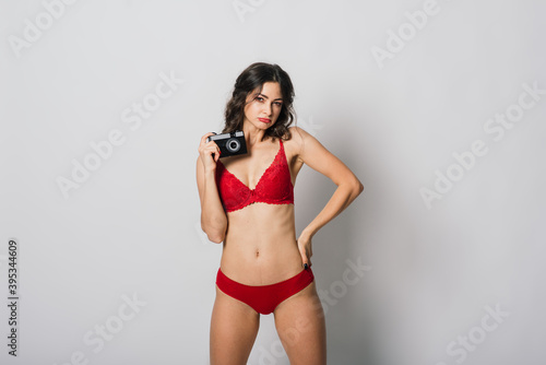 Beautiful female with pretty smile in red lingerie holding photo camera, isolated on white © Ivan Zelenin