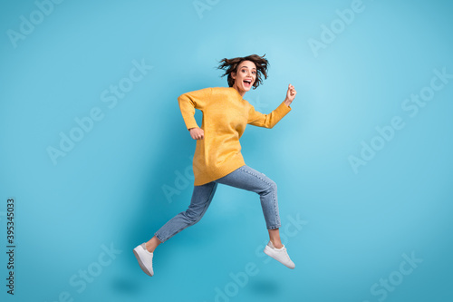 Full length body side profile photo of funny female runner laughing jumping up hurrying isolated on bright blue color background