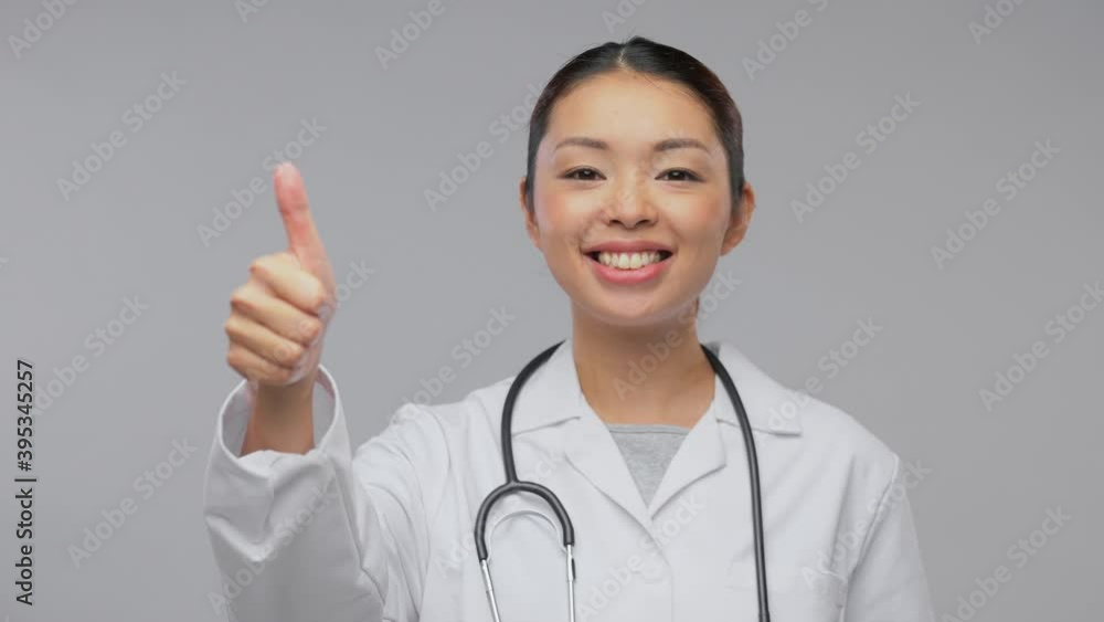 medicine, profession and healthcare concept - video portrait of happy smiling asian female doctor in white coat with stethoscope showing thumbs up over grey background medicine, profession and healthcare concept - video portrait of happy smiling asian female doctor in white coat with stethoscope showing thumbs up over grey background