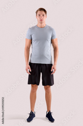 Full length portrait of young sporty guy in t-shirt and shorts standing on light studio background © Prostock-studio