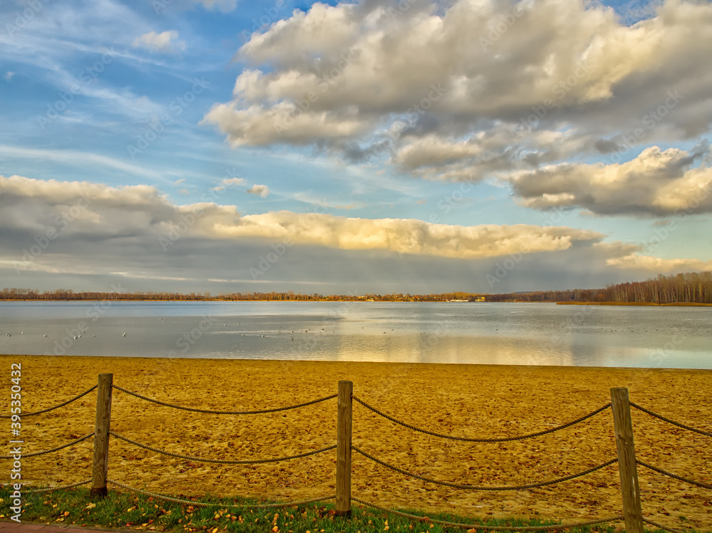 Fototapeta premium Beach at the Pogoria III Lake with sandy beach and clouds reflecting in water.