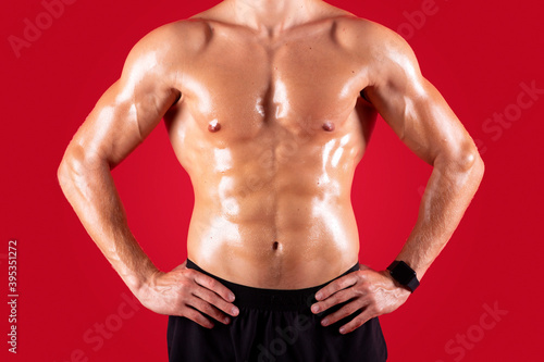 Cropped view of handsome young sportsman with bare torso posing with hands on hips over red studio background