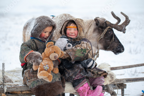 The Yamal Peninsula, the extreme north. Happy boy and girl on reindeer herder pasture in a cold winter day, polar circle, children and animals.