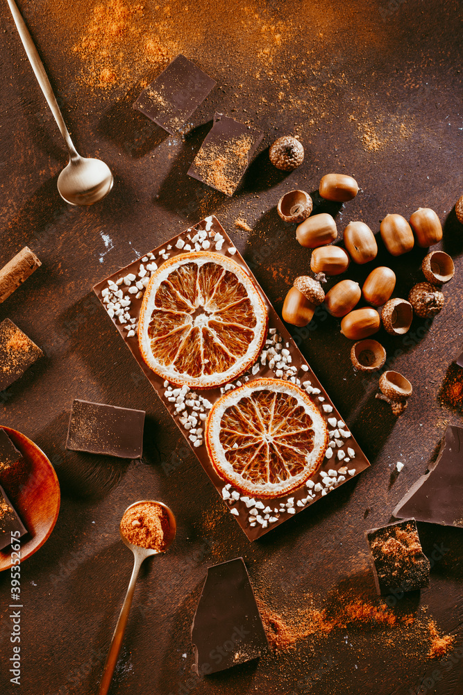 Composition of bars and pieces of different dark chocolate with orange slices, spices on a brown background close Composition of bars and pieces of different dark chocolate with orange slices, spices on a brown background close
