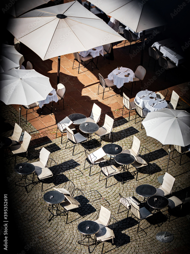 Fototapeta An overhead view of the empty tables and umbrellas of a street cafe in front of the cathedral in the tourist center of Strasbourg.