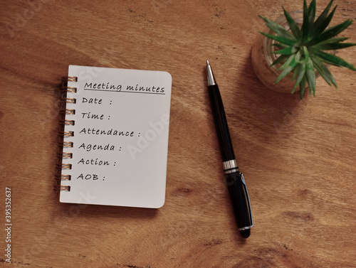 Meeting minutes list written on note pad with plant pot background and a pen