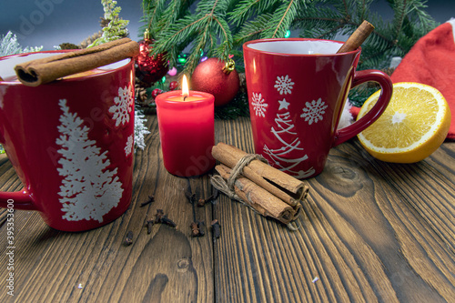 Two cups of aromatic hot mulled wine on a wooden table against the background of a Christmas tree with lights. Festive atmosphere concept. Selective focus.