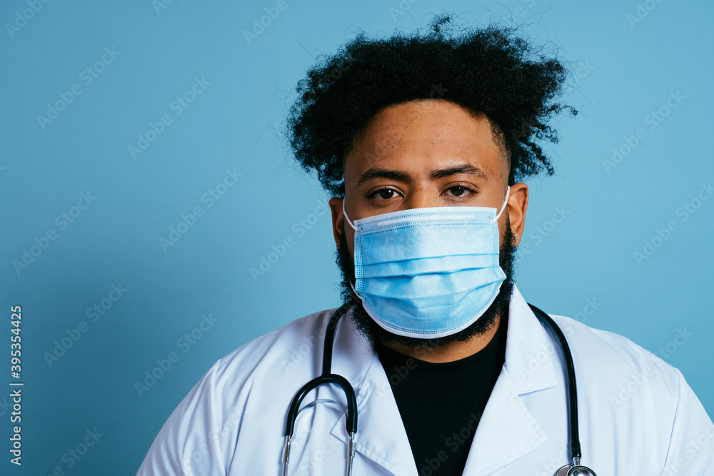 Portrait of a doctor in lab coat with face mask, isolated on blue background Portrait of a doctor in lab coat with face mask, isolated on blue background