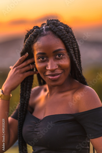 Lifestyle, Latina girl with black skin in a tight black short dress. On a mountain in a beautiful summer sunset