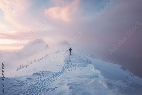 Fotografia Man mountaineer walking with footprint on snowy mountain and colorful sky in bli