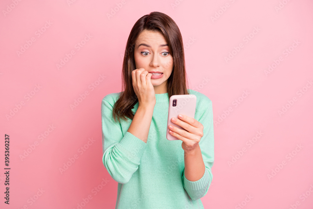 Photo of nervous girl hold cellphone gnaw nails look screen wear turquoise pullover isolated pink color background Photo of nervous girl hold cellphone gnaw nails look screen wear turquoise pullover isolated pink color background