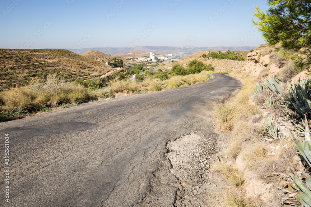 secondary paved road parallel to N-IIa road through a summer landscape approaching Fraga city, province of Huesca, Aragon, Spain