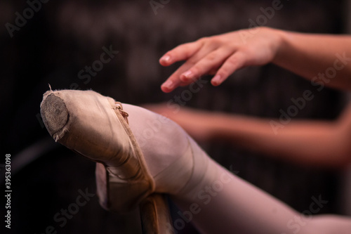 Ballerina has dance workout in ballet class room. Girl is stretching with leg in pointe shoes on barre. Woman is doing exercises.