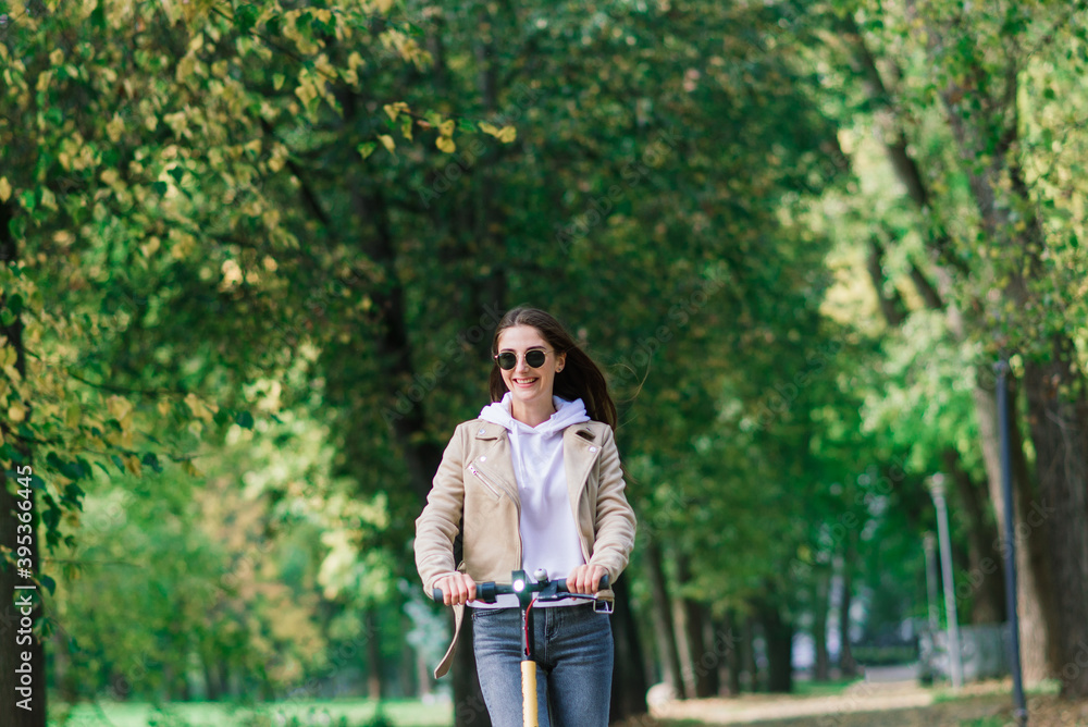 Young woman riding an electric scooter in an autumn park. Green transport, traffic jam problems.