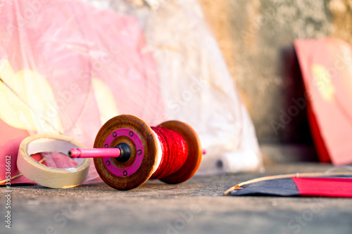 series of colorful red yellow paper and wood kits placed near fikri charki spools filled with dor plain thread and manjha glass covered thread for the indian festival of makar sankranti uttarayana