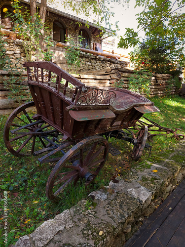Old horse cart made of brown wood and rusty iron. Traditional moldovan rural transport. Wooden fence and wall of stone background. Back view.