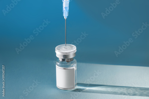 Fotografía Blue glass vial flask with liquid and syringe on a blue background with hard shadows
