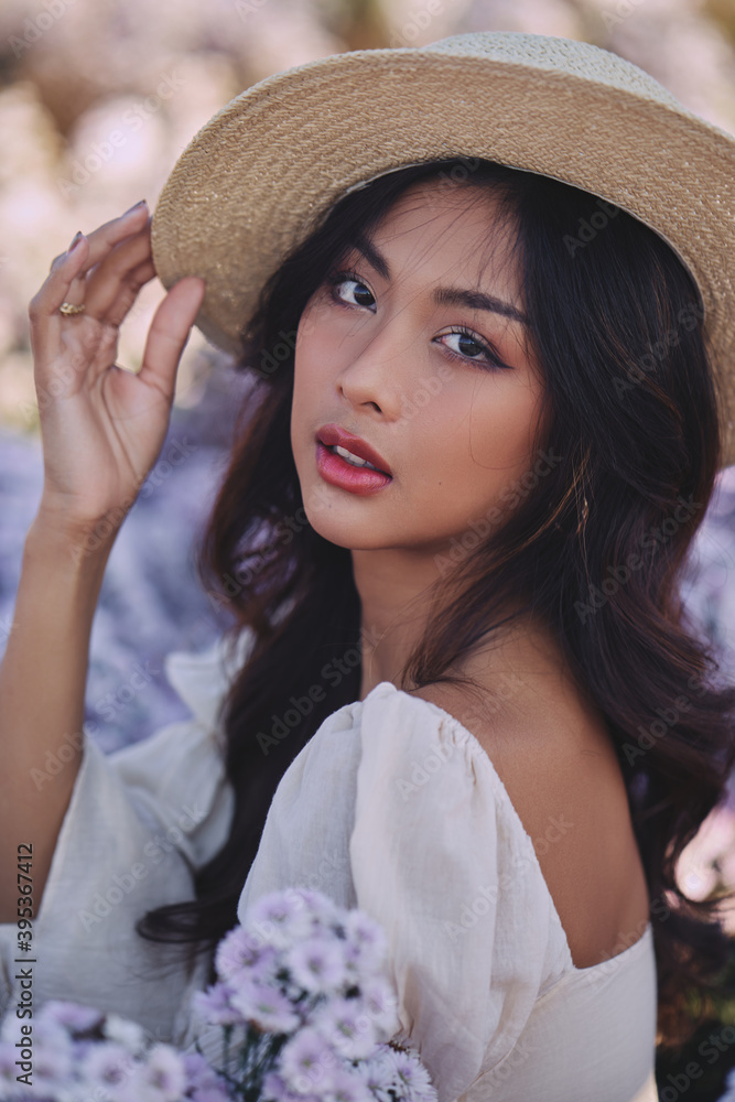 closeup fashion portrait of stylish young asian woman with straw hat posing at the purple flowers field