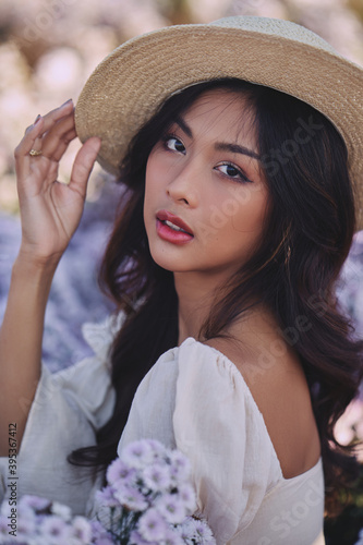Obraz na płótnie closeup fashion portrait of stylish young asian woman with straw hat posing at the purple flowers field w salonie