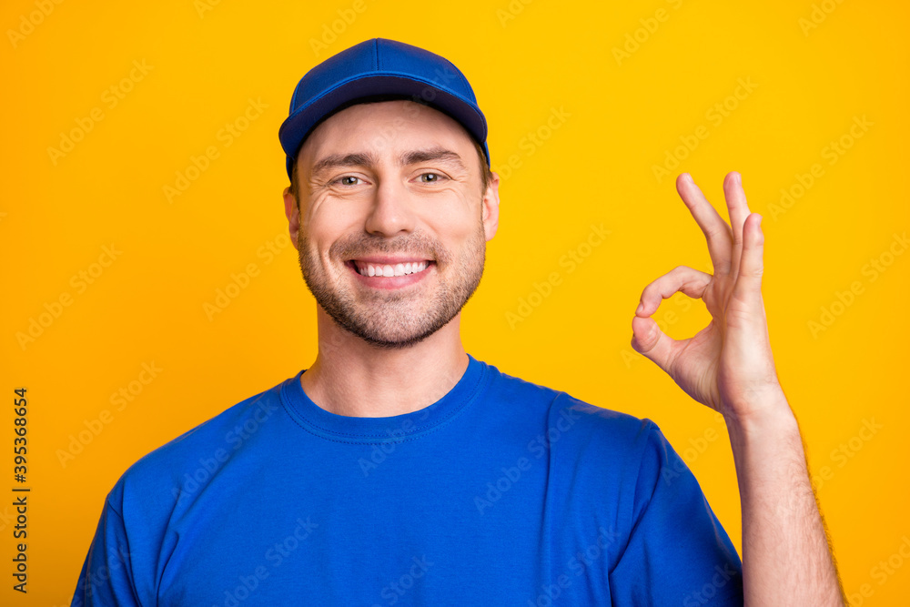Photo of friendly postman beaming smile fingers show okey symbol wear hat isolated on yellow color background Photo of friendly postman beaming smile fingers show okey symbol wear hat isolated on yellow color background