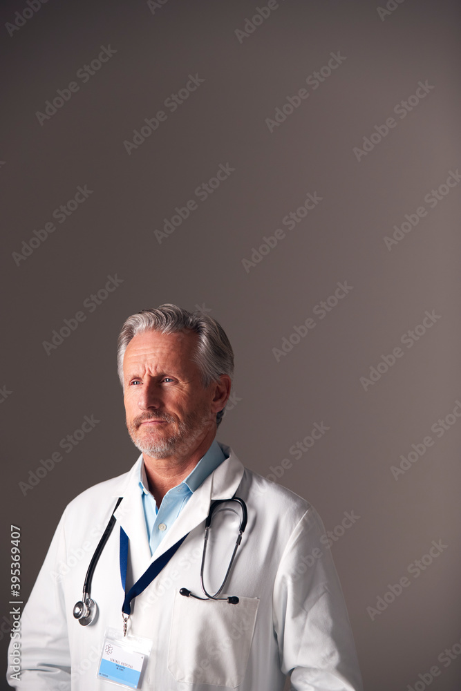 Studio Portrait Of Mature Male Doctor Wearing White Coat Standing Against Grey Background Studio Portrait Of Mature Male Doctor Wearing White Coat Standing Against Grey Background