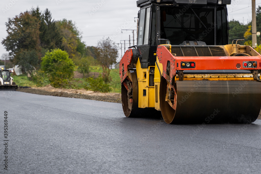 Asphalt road roller with heavy vibration roller compactor press new hot asphalt on the roadway on a road construction site. Heavy Vibration roller at asphalt pavement working. Repairing. Asphalt road roller with heavy vibration roller compactor press new hot asphalt on the roadway on a road construction site. Heavy Vibration roller at asphalt pavement working. Repairing.