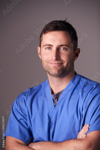 Studio Portrait Of Male Nurse Wearing Scrubs Standing Against Grey Background