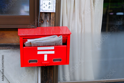 closed up the japanese red mailbox, Many japan newspapers are hanging from old post box in front house.