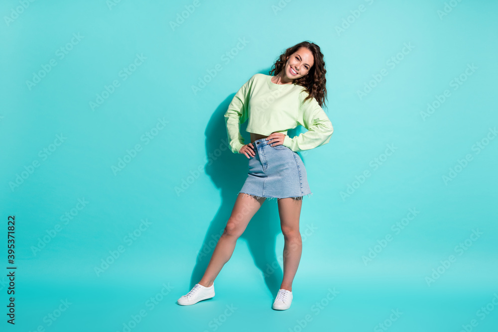Full length body size photo of young pretty girl wearing casual jeans skirt and green crop smiling isolated on bright teal color background Full length body size photo of young pretty girl wearing casual jeans skirt and green crop smiling isolated on bright teal color background