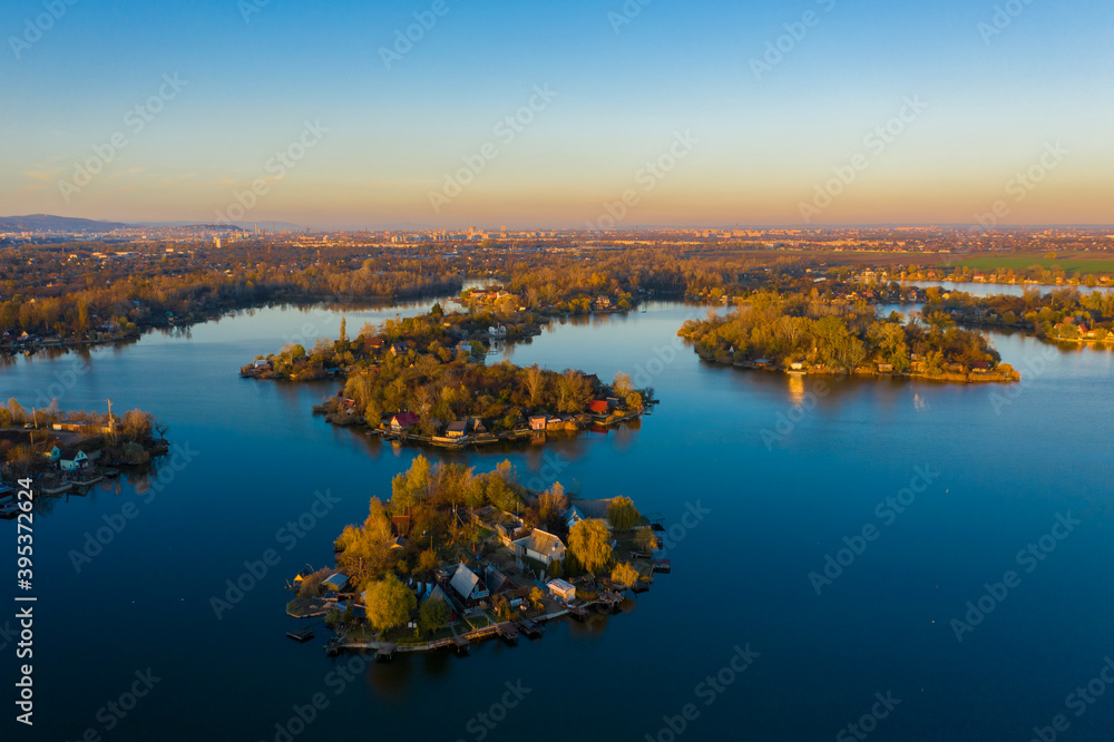 Fototapeta premium Szigetszentmiklós, Hungary - Aerial drone view of a tiny fishing island on Lake Kavicsos (Kavicsos to) near Budapest. The island is full with fishing huts, piers and cabins. Warm autumn colors.
