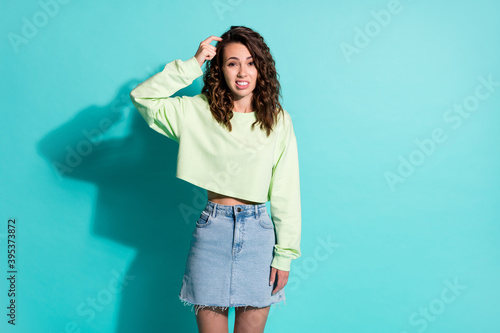 Photo portrait of confused woman scratching head with finger isolated on vivid teal colored background