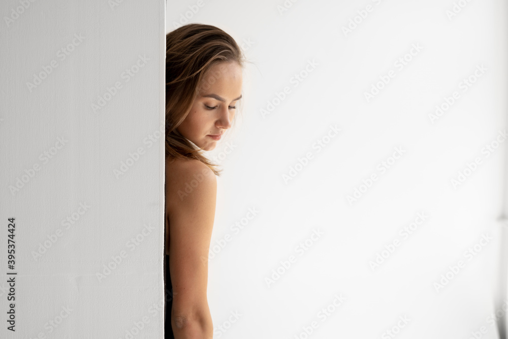 Portrait of young brunette skinny woman is posing in black underwear and standing behind a white wall in white studio. Model tests of pretty girl in basic clothes on cyclorama. Portrait of young brunette skinny woman is posing in black underwear and standing behind a white wall in white studio. Model tests of pretty girl in basic clothes on cyclorama.