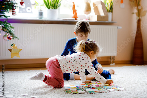 Two little chilren, cute toddler girl and school kid boy playing together card game by decorated Christmas tree. Happy healthy siblings, brother and sister having fun together. Family celebrating xmas photo