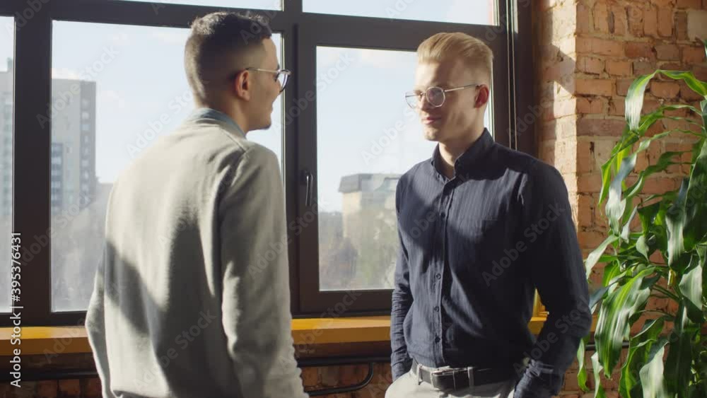 Medium shot of biracial successful business partners greeting each other smiling and shaking hands in bright office with panoramic windows Medium shot of biracial successful business partners greeting each other smiling and shaking hands in bright office with panoramic windows