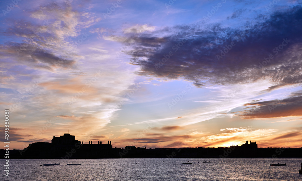 Image of Elizabeth Castle in silhouette at sunset with clouds and sea in the foreground. Jersey CI