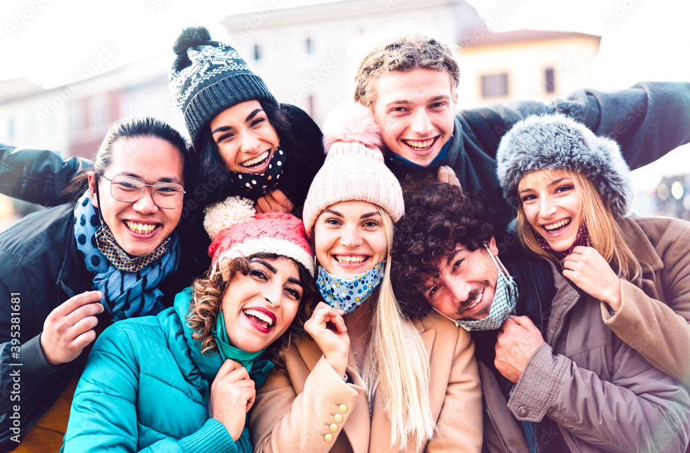 Multiracial friends taking selfie with open face mask and winter clothes - New normal friendship concept with milenial people having fun together outside - Bright filter with focus on central woman - obrazy, fototapety, plakaty 