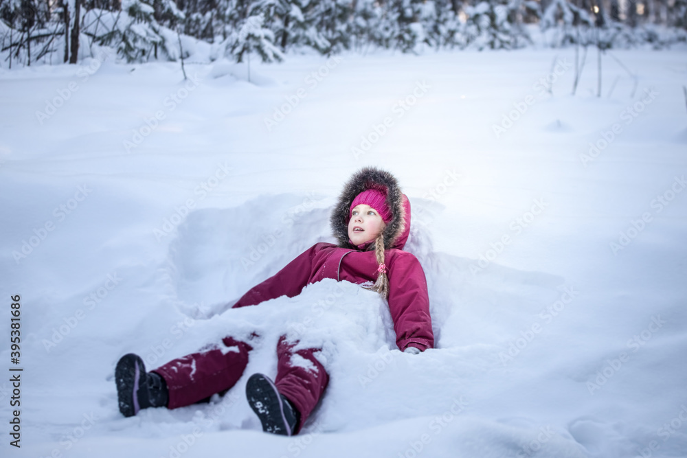 A girl in a red jumpsuit sits on the snow and looks with hope and surprise into the distance against the background. The concept of the winter holidays. A girl in a red jumpsuit sits on the snow and looks with hope and surprise into the distance against the background. The concept of the winter holidays.