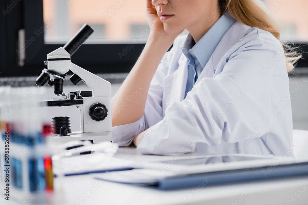 cropped of scientist leaning on hand near microscope in lab cropped of scientist leaning on hand near microscope in lab