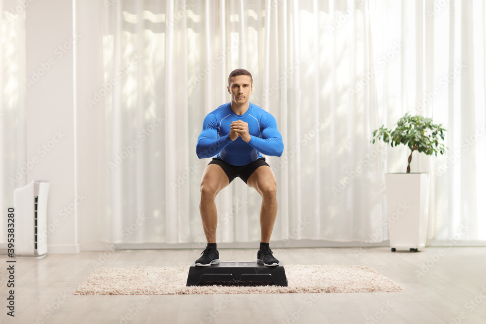 Fit muscular young man doing squat exercise on a step aerobic platform Fit muscular young man doing squat exercise on a step aerobic platform