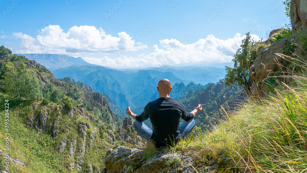 Strong young man sitting on the edge of a cliff admiring the mountain landscape. A man over a mountain precipice. Mountain peaks of the North Caucasus.