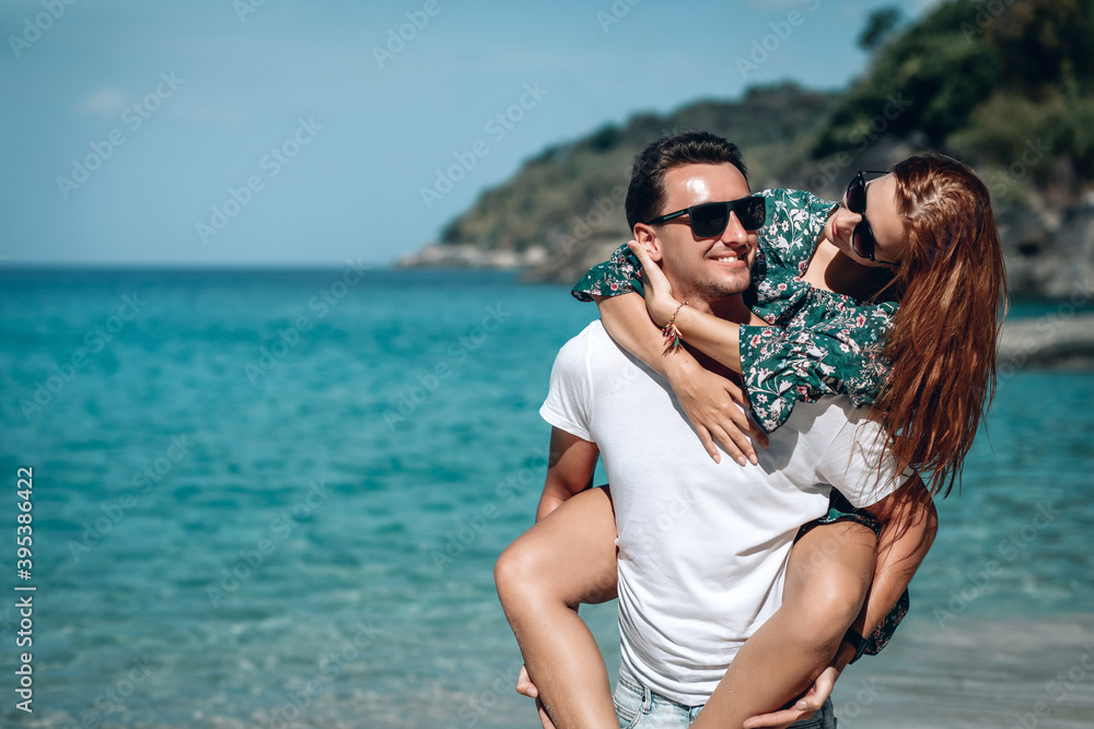 Caucasian man carrying his red haired girlfriend on his back while enjoying a late afternoon together at the beach. Phuket. Thailand. Caucasian man carrying his red haired girlfriend on his back while enjoying a late afternoon together at the beach. Phuket. Thailand.