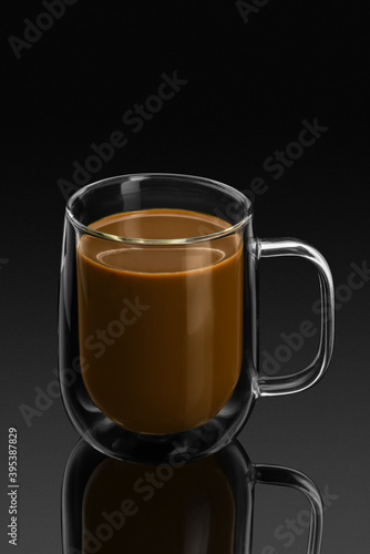 double wall glass mug with coffee on a black background with reflection