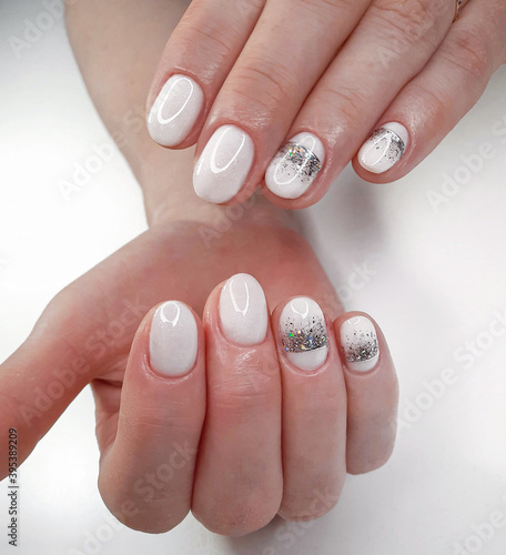 White nails with sequins and a silver crown design on a white background. White shiny gel polish on round short nails