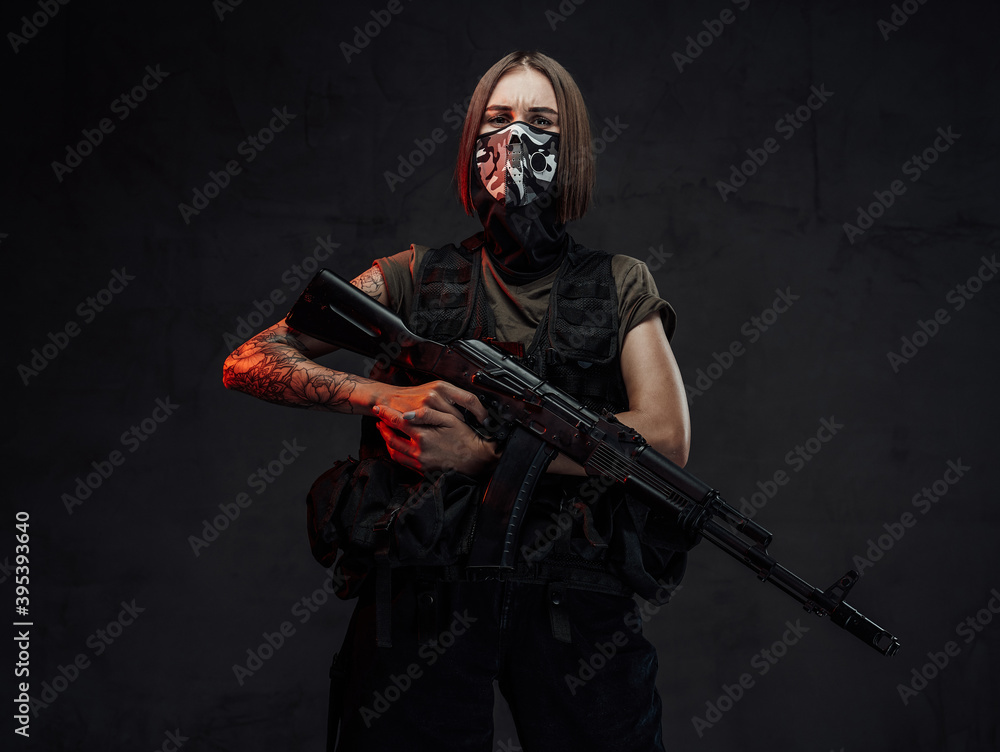 Armed with ak74 rifle and weared with mask stylish female mercenary poses in dark background. Armed with ak74 rifle and weared with mask stylish female mercenary poses in dark background.