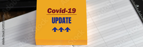 COVID-19 UPDATE text on yellow sticker on desktop background, banner format.
