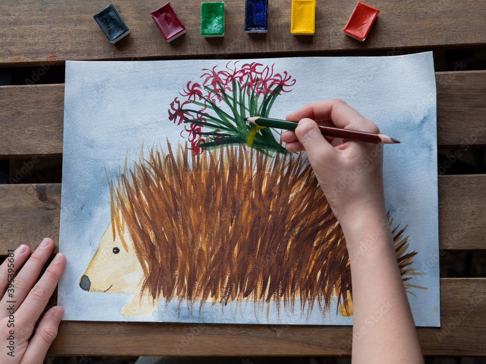 little girl draws a hedgehog with watercolors and pencils