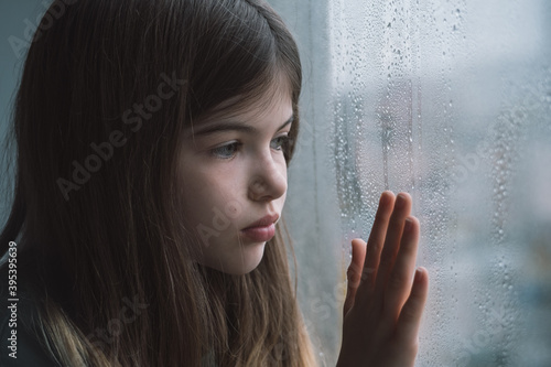 little, young sad girl at the window. Keeps his hand on the glass, lonely child depressed