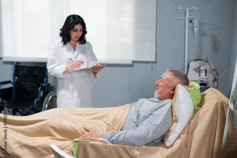 A doctor making some notes in the report on her clipboard, while visiting her patient in the ward. Healthcare concept. A doctor making some notes in the report on her clipboard, while visiting her patient in the ward. Healthcare concept.