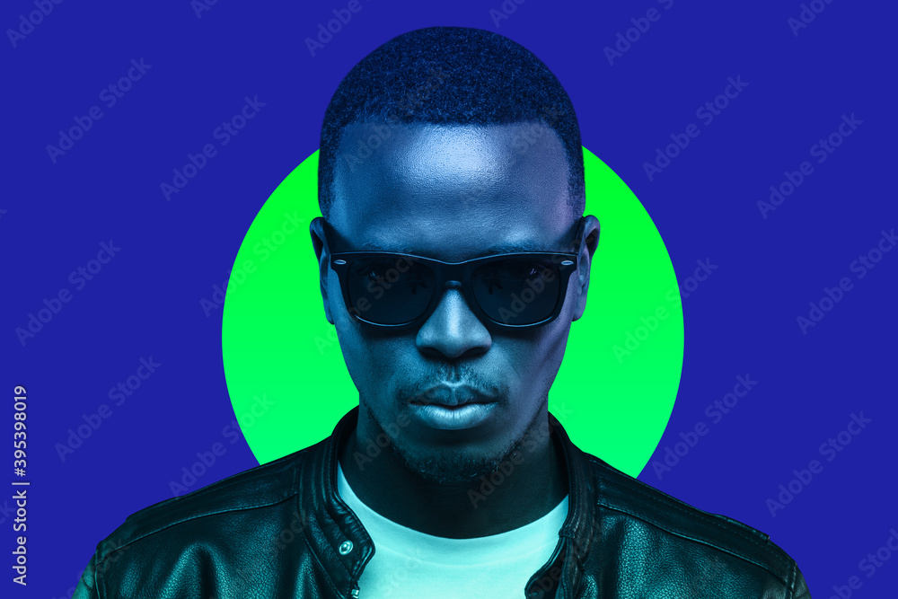 Studio portrait of african american man wearing sunglasses and leather jacket isolated on blue background